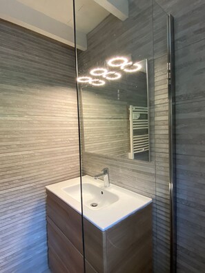 A modern bathroom with a glass partition, a white sink, and a mirror reflecting a towel rack.