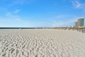 Une plage avec un filet de volley-ball, une étendue de sable et un immeuble de grande hauteur en arrière-plan.