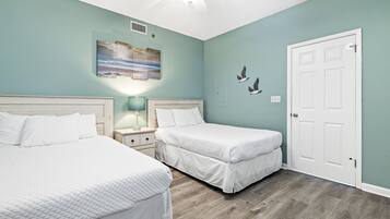 Une chambre avec deux lits, un ventilateur de plafond, un tableau et une porte blanche.