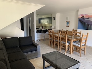 Un soggiorno con un divano nero, un tavolo da pranzo con sedie in legno e una cucina sullo sfondo.