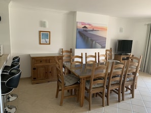 Zona pranzo con un tavolo e sedie in legno, una televisione e un quadro raffigurante un molo.