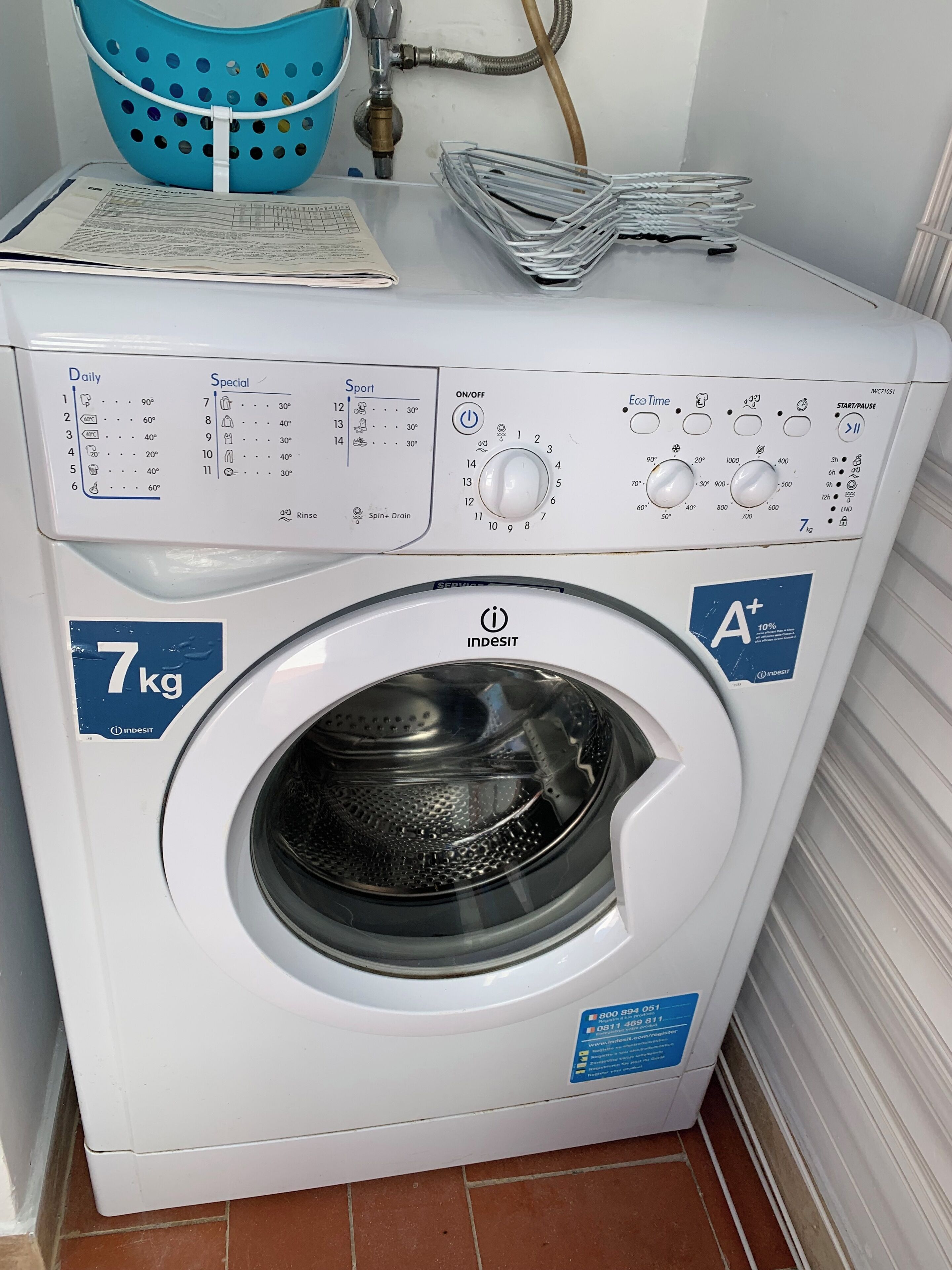 Lavadora de carga frontal con etiqueta de capacidad de 7 kg, panel de control con diversas opciones y manguera de entrada de agua.