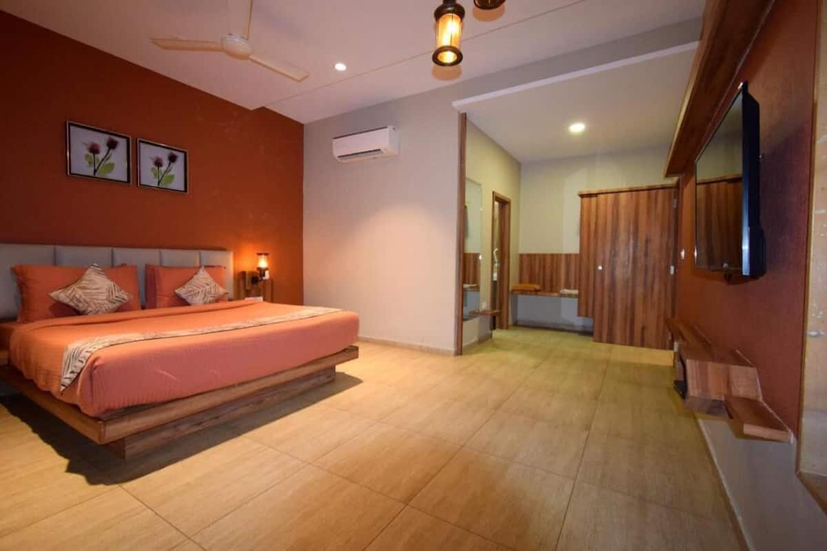 A bedroom with a bed, bedside lamps, a ceiling fan, an air conditioning unit, and a wooden wardrobe.