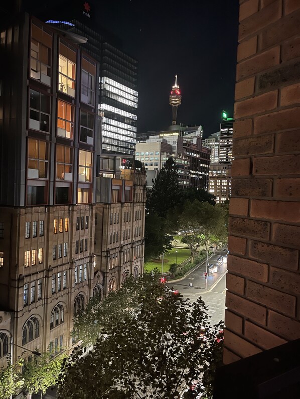 Un paisaje urbano nocturno con edificios modernos e históricos, una torre destacada con luz roja y una calle con vehículos.