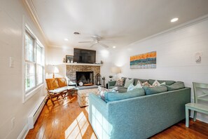 A living room with a fireplace, a sofa, a dining area, and a ceiling fan. - Tranquil Lake Hideaway w/ Dock & Hot Tub (Oakland)