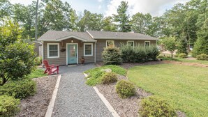 A single-story house with a front porch, a red chair, and a gravel driveway.