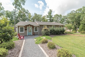 A single-story house with a front porch, a red chair, and a gravel driveway.