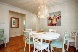 A dining area with a round table, white chairs, and a hanging light fixture.