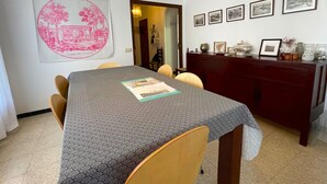 Un coin repas avec une table recouverte d’une nappe à motifs, des chaises, un luminaire suspendu et des tableaux encadrés accrochés au mur.