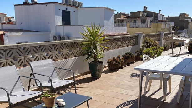Une terrasse sur le toit avec des sièges extérieurs, un pot de fleurs et un auvent rayé.