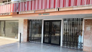 A building entrance with a metal gate, a tiled floor, and a balcony with red curtains.
