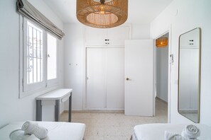 Habitación de hotel con cama, mesita de noche, armario, espejo y ventana con cortina.
