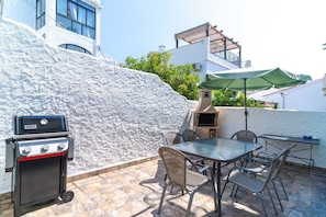 Eine Terrassengaststätte mit Grill, Tisch, Stühlen und einem Barbecue-Ofen.