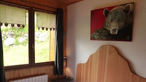 Una habitación de madera con una cama, un ventanal con cortinas, un radiador y un cuadro de un oso en la pared.