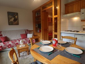 A cozy living room with a sofa, a dining table set for two, and a kitchen area with a stove.