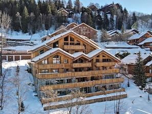 A multi-story wooden lodge with balconies, surrounded by snow-covered trees and other lodges.