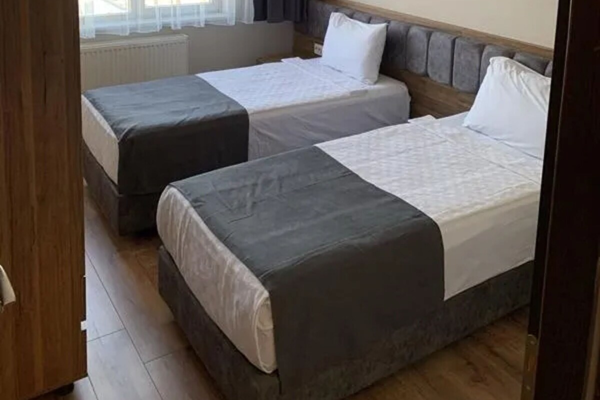 Una habitación con dos camas, una ventana con cortinas, un radiador y un armario de madera.