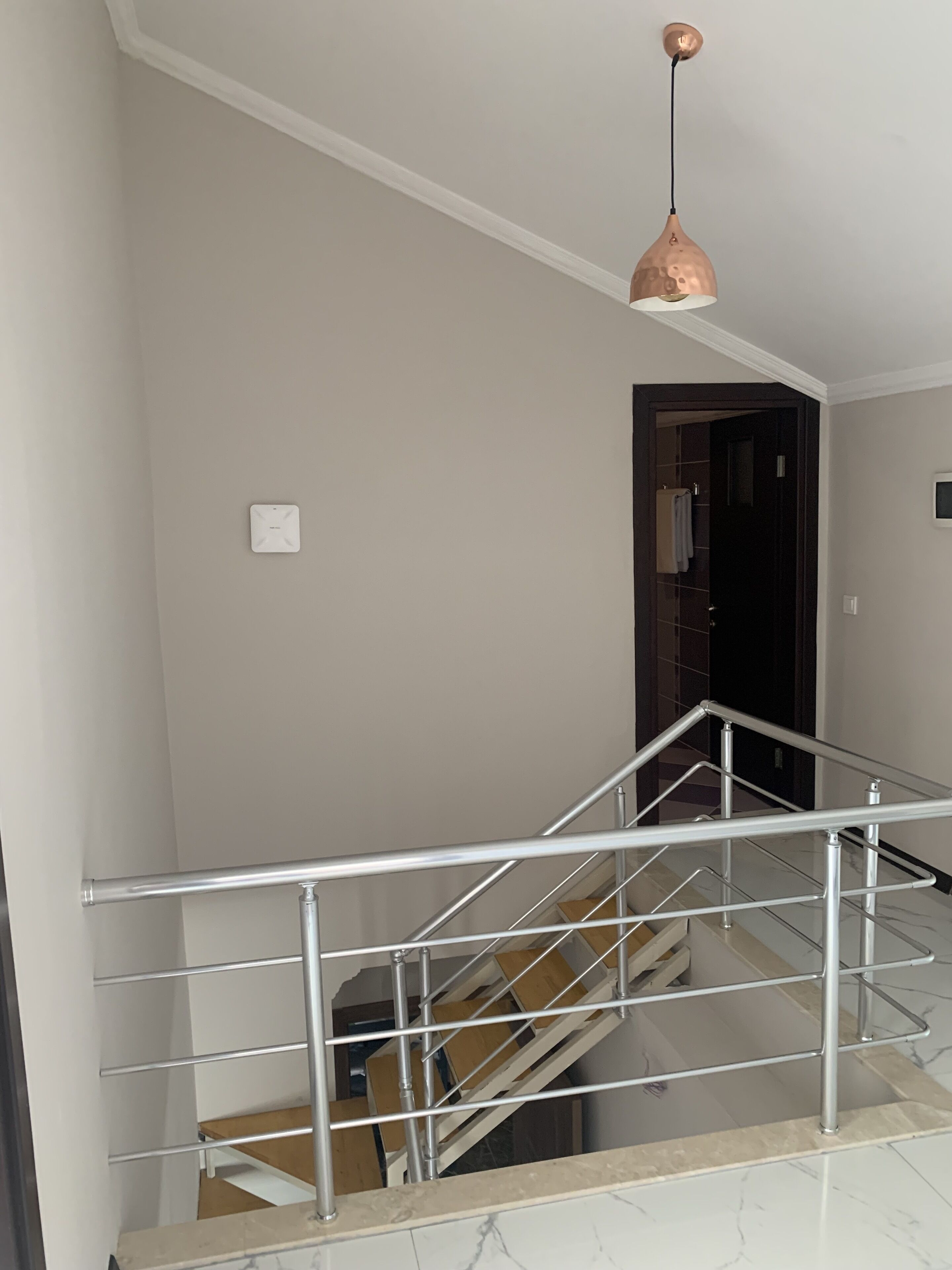 Una escalera con barandilla de metal, una lámpara colgante de cobre y una pared blanca.