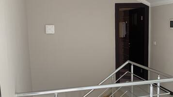 Una escalera con barandilla de metal, una lámpara colgante de cobre y una pared blanca.