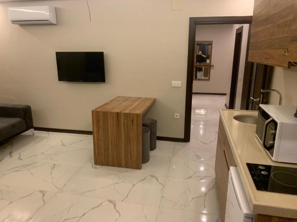 A modern living room with a flat-screen TV, a wooden coffee table, and a marble floor.
