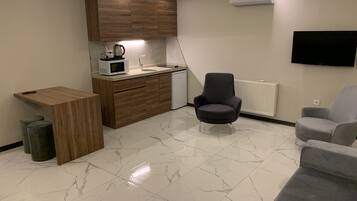 Eine moderne Küche mit Holdekor, einer weißen Arbeitsplatte und einer eingebauten Mikrowelle. Ein grauer Sessel und ein kleiner Tisch mit Papierkorb sind ebenfalls vorhanden.