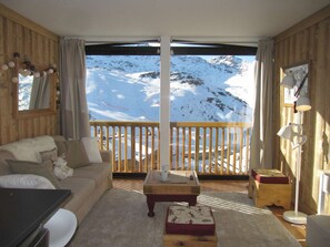 Una habitación acogedora con detalles de madera, un amplio ventanal con vistas a una montaña nevada, una mesa de centro de madera y un sofá con una manta suave.