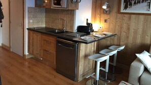 A compact kitchen with wooden cabinetry, a built-in microwave, a dishwasher, and a small bar area with stools.