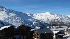 A snow-covered mountain with a clear sky. There are buildings with snow on their roofs in the foreground.