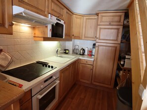 Uma cozinha compacta com armários de madeira, fogão, forno, pia e micro-ondas.
