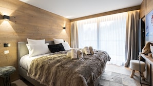 A modern bedroom with a wooden headboard, a large bed with a fur throw, a small stool, and a television on a wooden stand. - Beautiful 76m² apartment in Courchevel, near slopes, 3 bedrooms, parking (Courchevel 1550)