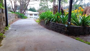 A paved pathway leading to a building with a brick wall on one side and a row of green plants. - GreenLeaf Retreat@Katoomba/BMountains-Pets Welcome (Wentworth Falls)