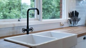 Una cocina con un lavamanos doble, una ventana con vista a árboles y un bloque de cuchillos en la encimera.