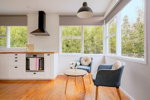 A modern kitchen with white cabinetry, a built-in oven, and a large window overlooking greenery.