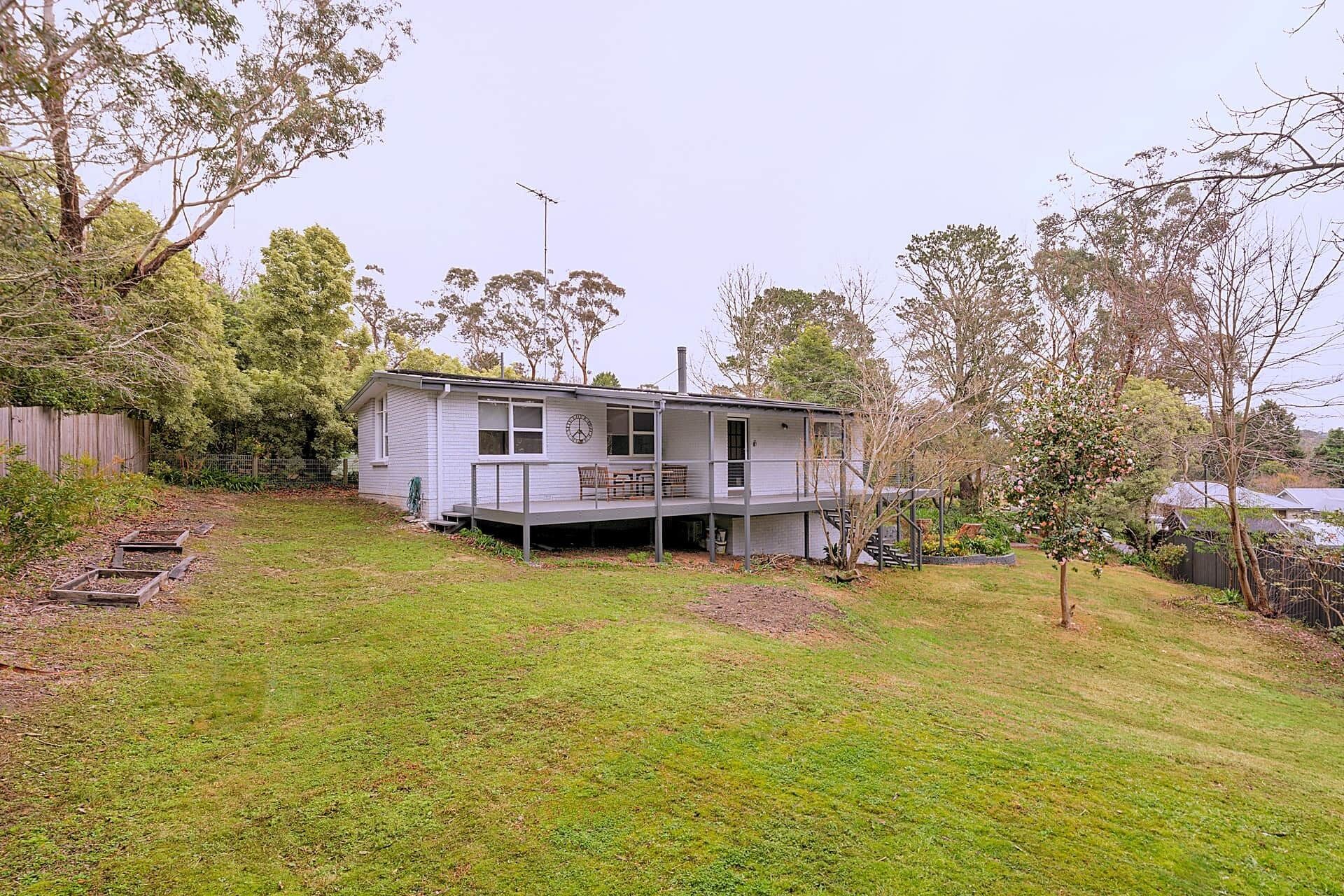 A two-story house with a balcony, surrounded by a grassy yard and trees.
