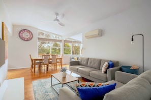 A living room with a sofa, coffee table, and a dining area with chairs. - GreenLeaf Retreat@Katoomba/BMountains-Pets Welcome (Wentworth Falls)