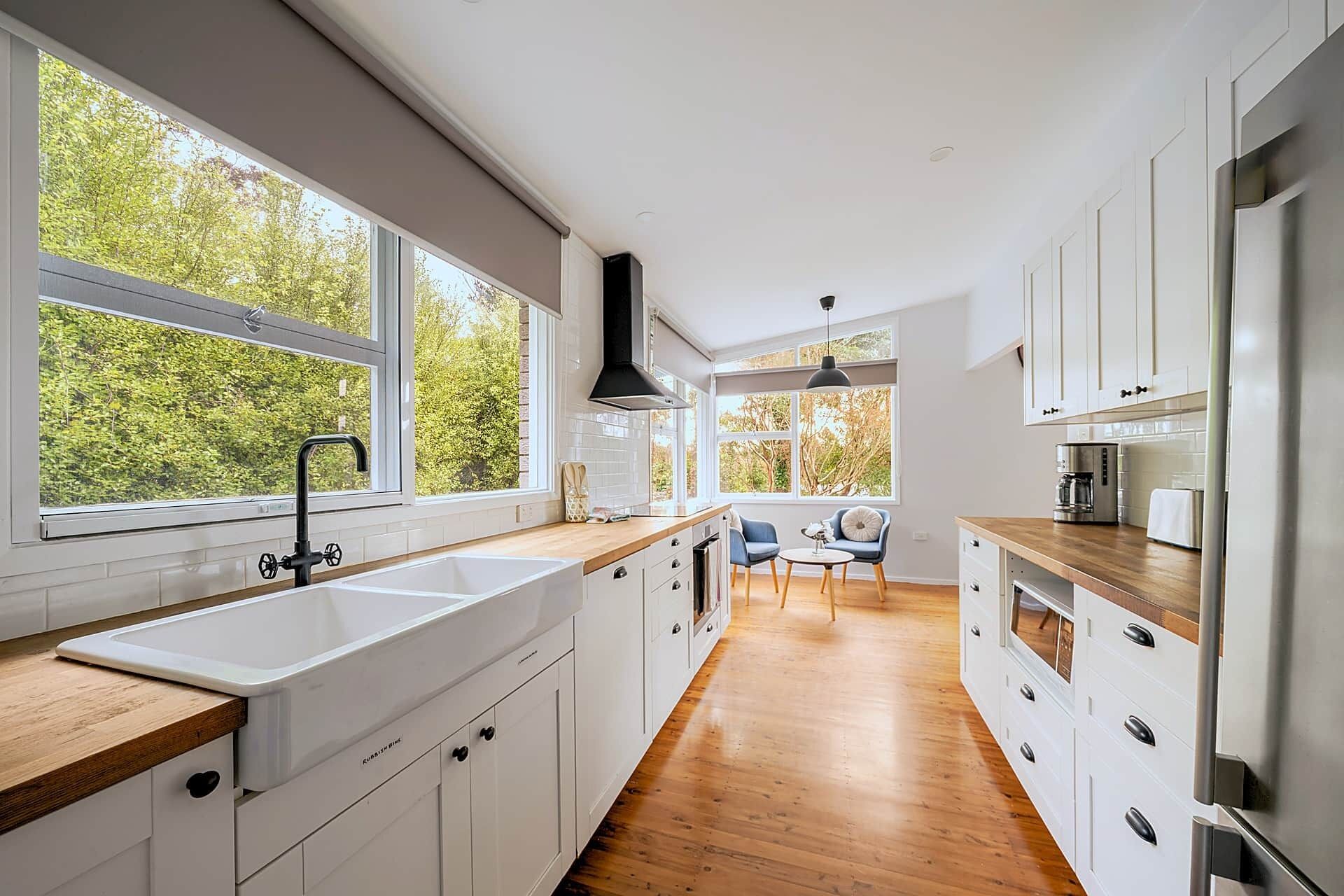 Une cuisine moderne avec des meubles blancs, un plan de travail en bois et une grande fenêtre donnant sur un jardin.