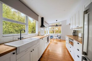 A modern kitchen with white cabinets, a wooden countertop, and a large window overlooking a garden.