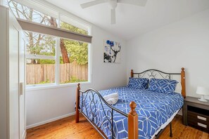Un dormitorio con cama, ventana, ventilador de techo y suelo de madera.