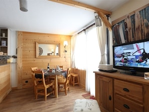 Um quarto acolhedor com uma mesa de jantar de madeira posta para quatro pessoas, uma televisão em um suporte de madeira e um espelho grande na parede.