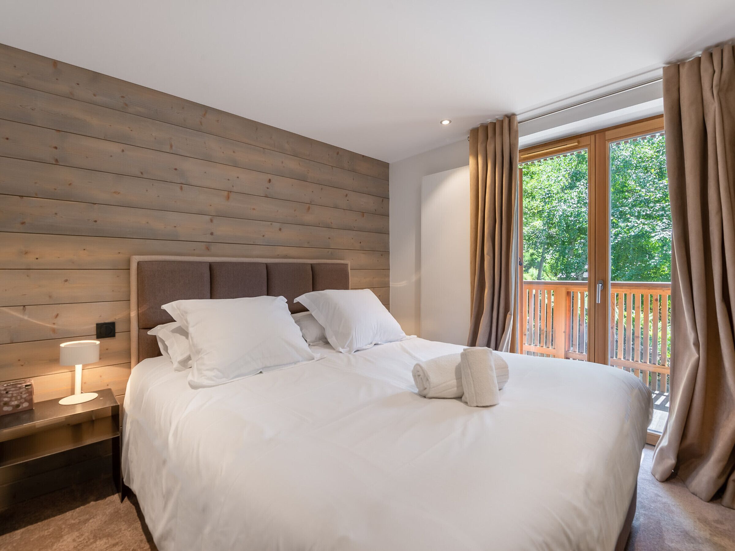 A neatly made bed with white linens, a wooden headboard, and a nightstand with a lamp.