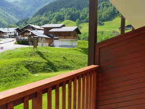 Un balcon en bois donnant sur un village avec des maisons traditionnelles, un restaurant et une vue dégagée sur les collines environnantes.