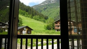 A view from a window overlooking a green valley with houses and mountains in the background.