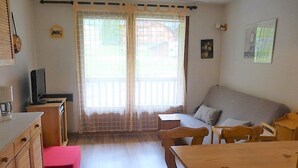 A cozy room with a wooden table, a sofa, and a TV on a small cabinet.
