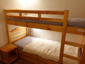 A bunk bed with a wooden frame, a small bedside table, and a light source above the bed.