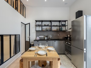 Uma cozinha moderna com uma mesa de jantar de madeira para quatro pessoas, uma geladeira de aço inoxidável e um armário preto acima do balcão.