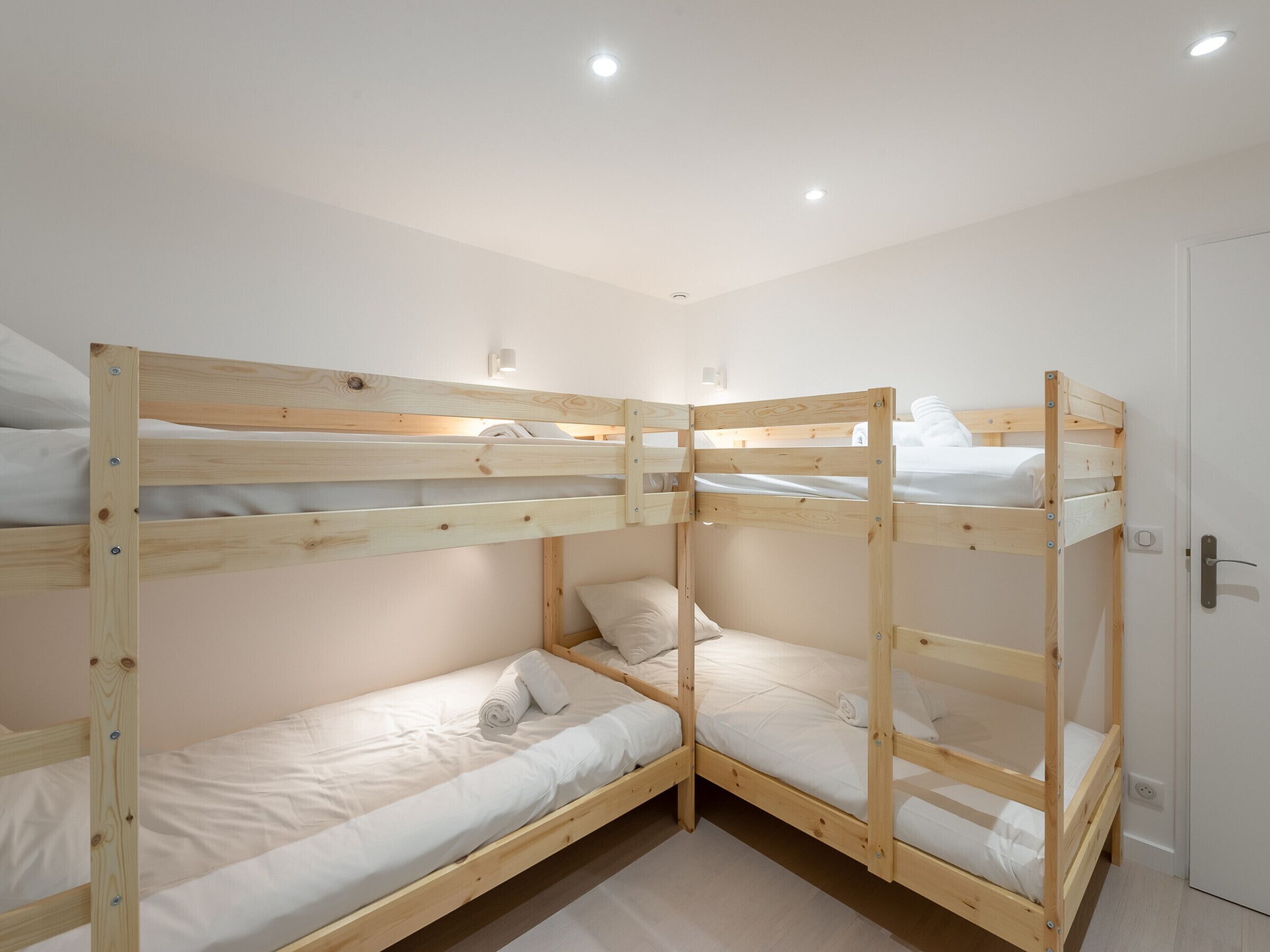 Een slaapkamer met een stapelbed van drie hoogtes, witte beddengoed en een deur met een greep.