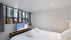 A hotel room with a bed, a TV on a wooden stand, and a window with curtains.