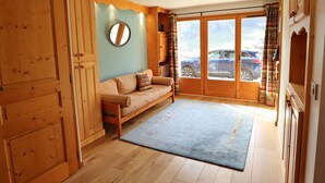 A cozy room with a wooden floor, a sofa, a rug, and a large window with curtains. - Family Chalet: Sleeps 10, Near Village & Slopes, WiFi, Fireplace, BBQ, Game Room (Arêches-Beaufort)