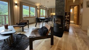 A spacious living area with a fireplace, dining table, and comfortable seating. Large windows offer a view of the outdoors. - Contemporary chalet for 8, 4 bedrooms, mountain views, parking, near village (Arêches-Beaufort)