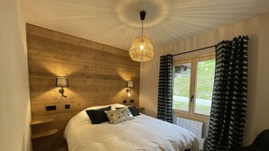 A bedroom with a wooden headboard, two bedside lamps, a large bed with pillows, a window with curtains, and a chair. - Contemporary chalet for 8, 4 bedrooms, mountain views, parking, near village (Arêches-Beaufort)